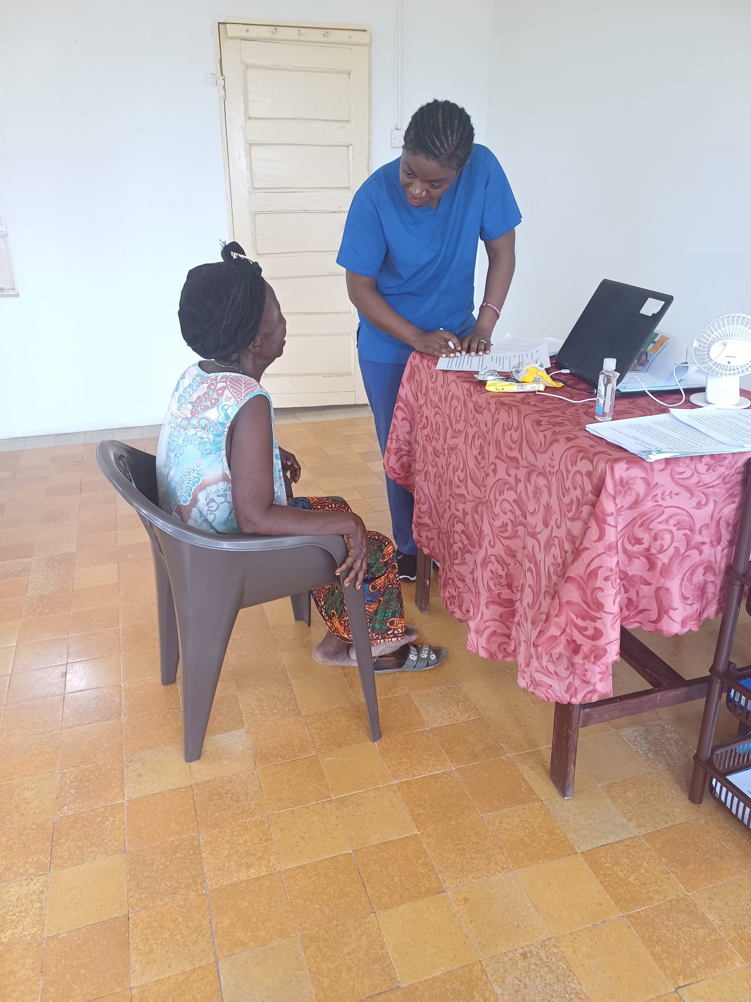 Adama, our co-founder, assisting a sitting elderly woman who is unable to read and write with her consent form.