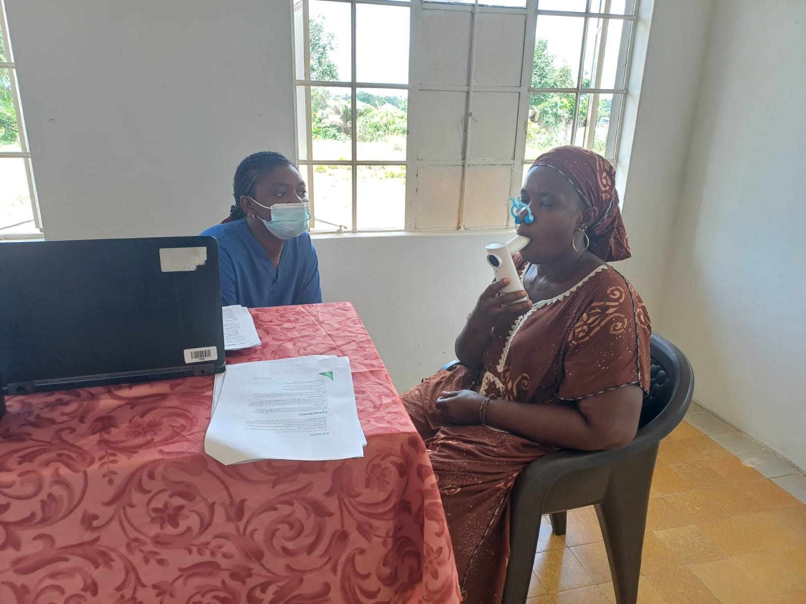 A female participant is using a portable spirometer as part of a lung function test, assisted by Adama, our co-founder.