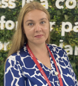 Kseniia, a white woman with long blonde hair wearing a blue and white shirt and a red lanyard, is smiling at the camera.